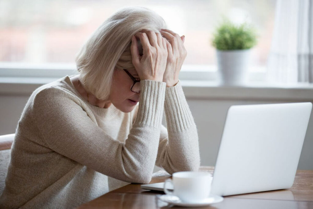 middle aged woman rests her head in her hands in front of a computer wondering why is life so hard