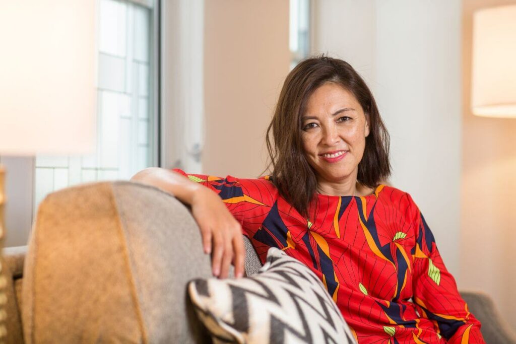 happy middle aged woman in a pretty red shirt sits on a sofa and smiles