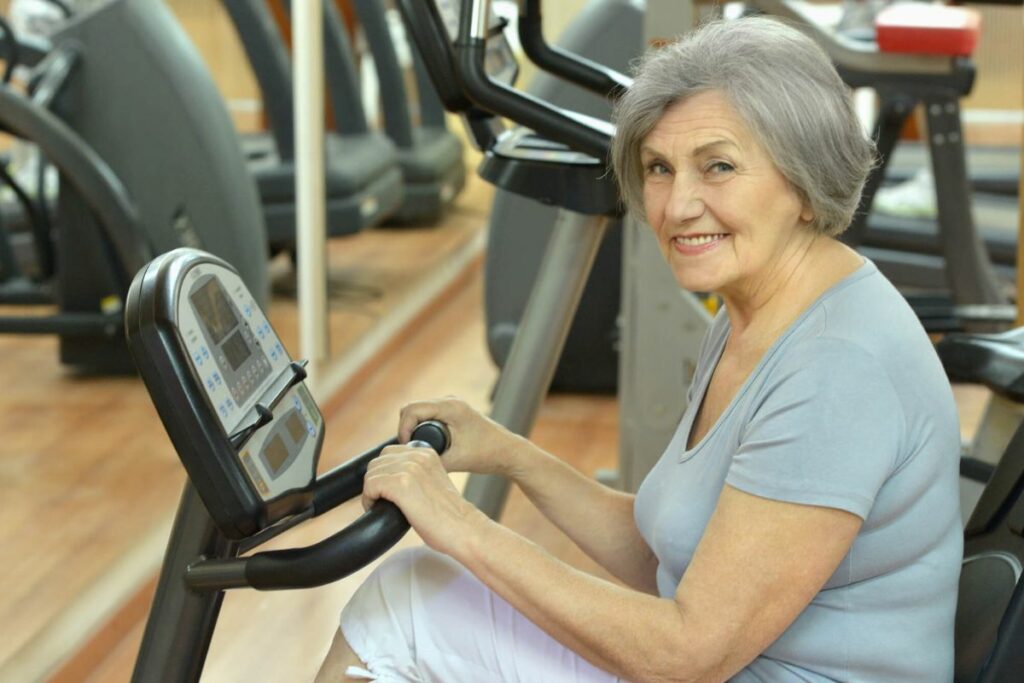 a senior female uses a stationary bicycle in a senior center gym