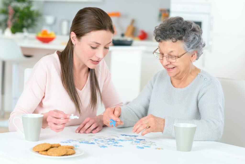 a senior woman and her adult granddaughter enjoy putting a puzzle together