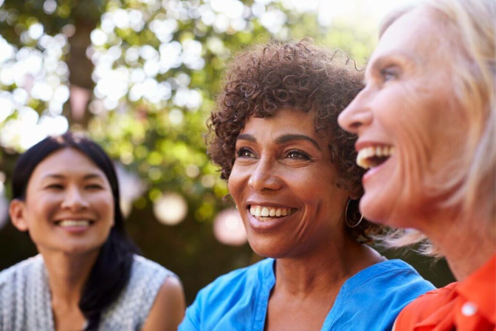 three girlfriends over 50 laugh and smile about something off in the distance