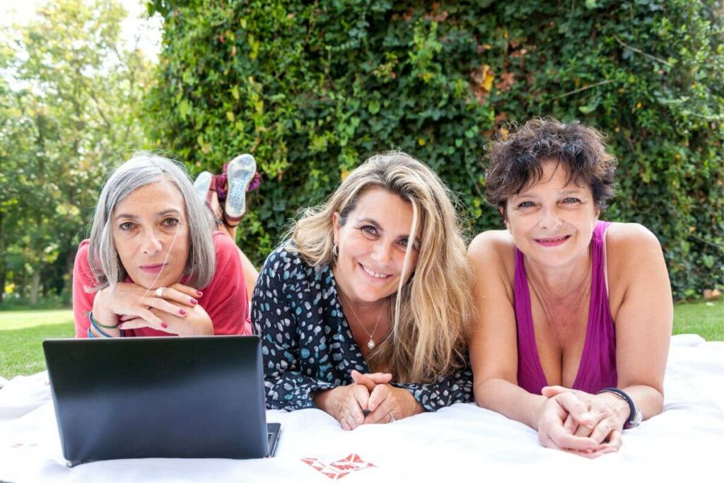 three girlfriends over 50 lay on a blanket in the park together and reminisce about good times