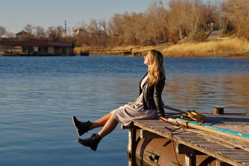 woman siting on a dock by the water prioritizing herself and her self care needs