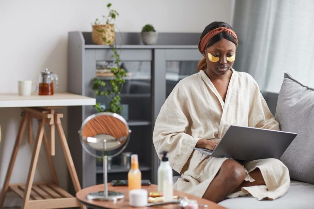 beautiful woman works on her laptop in a comfortable environment at home while doing facial self care in her robe