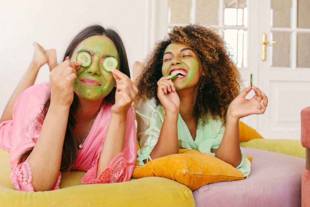 two young women do facials as as they lay on cushions laughing together