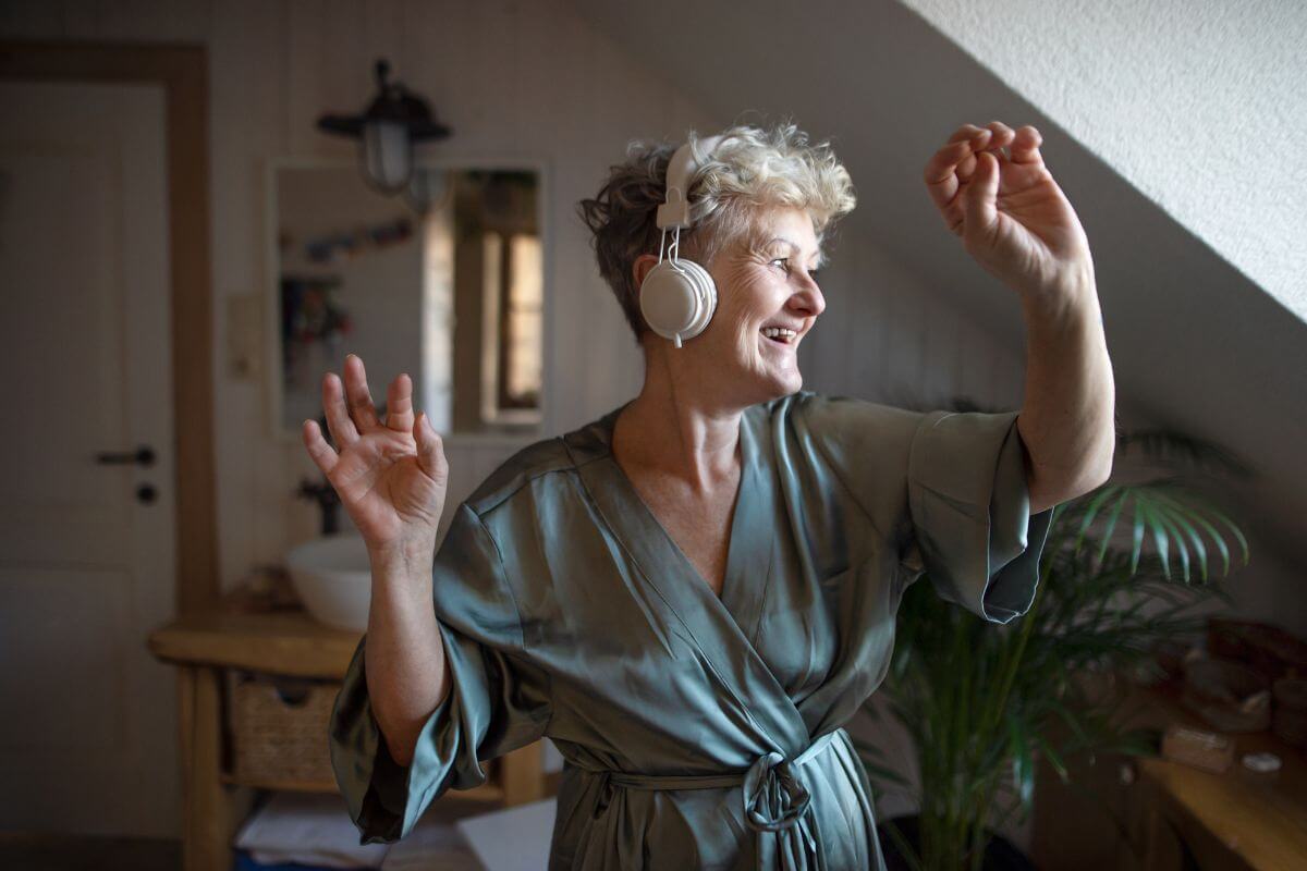 middle aged woman with headphones on happily dances to her favorite music on a self care weekend