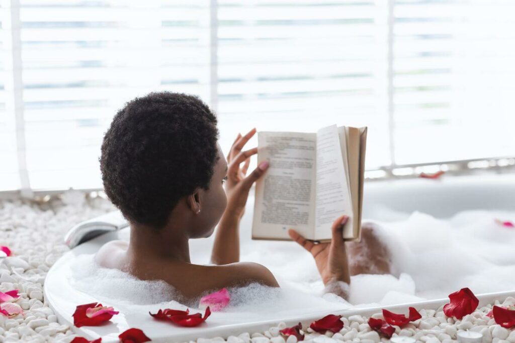 a young woman sits in a bubble bath reading her favorite book on a self care weekend