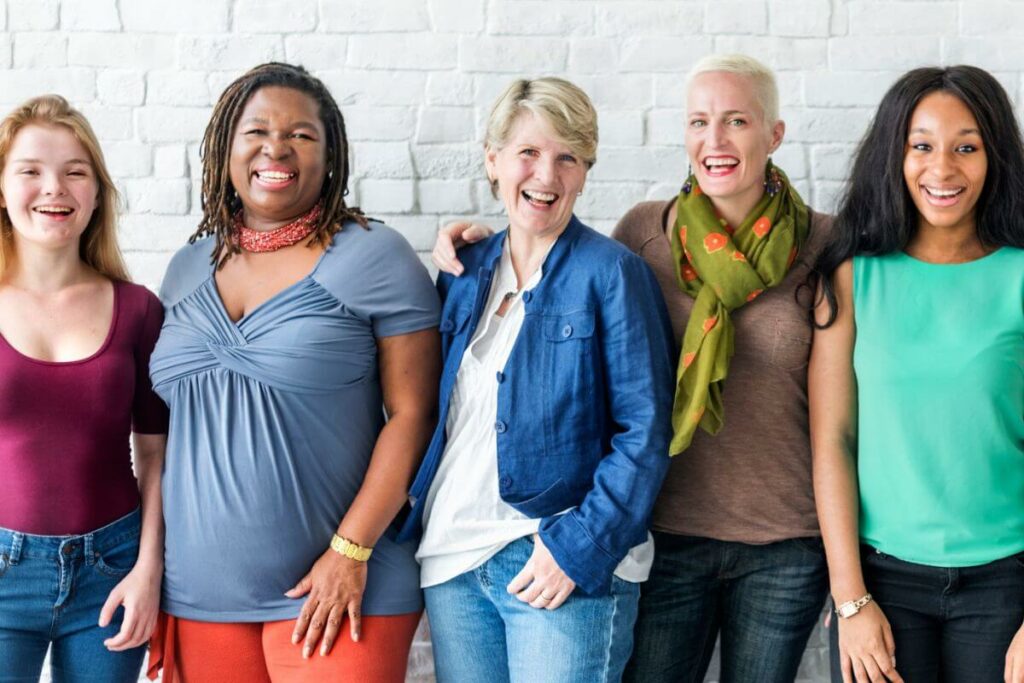 a lively group of five women wearing a variety of casual clothes smile at the camera