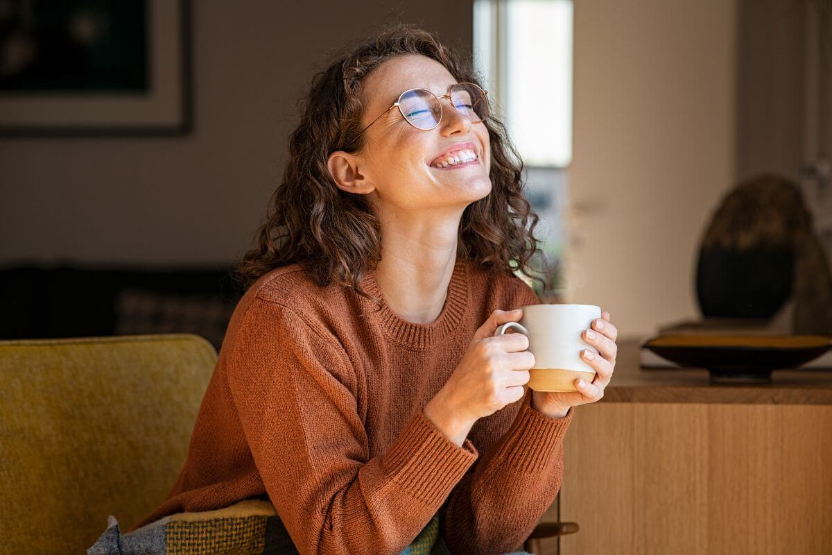 very happy woman sits on her sofa with a cut of tea after saying her affirmations for letting go