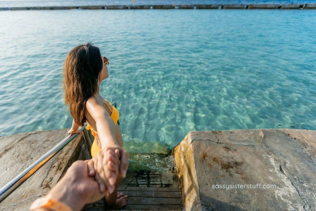 beautiful woman steps down a staircase into a beautiful blue body of water