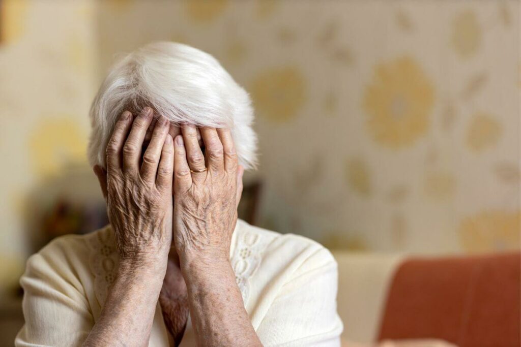 a distraught elderly person with dementia covers her face with her hands