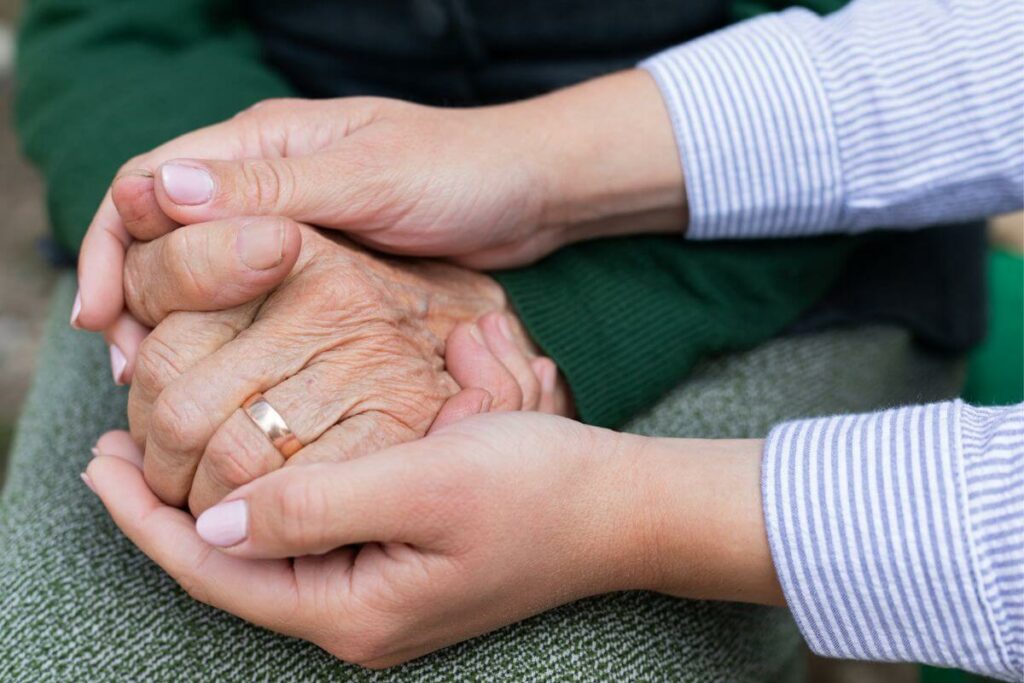 a close up of an adult child holding the hands of an elderly parent