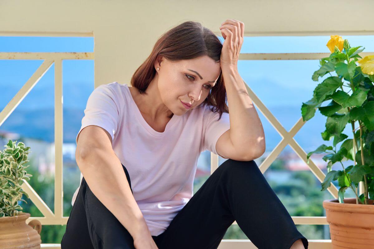 middled aged woman sits with her hand to her forehead looking defeated