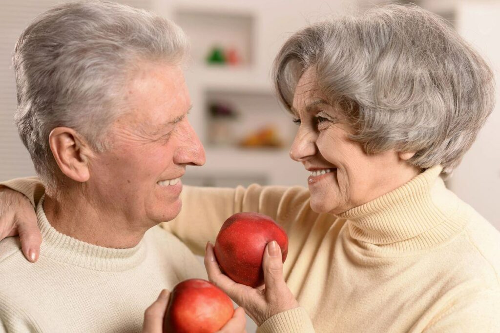 a happy senior couple eating healthy as they hug and enjoy apples