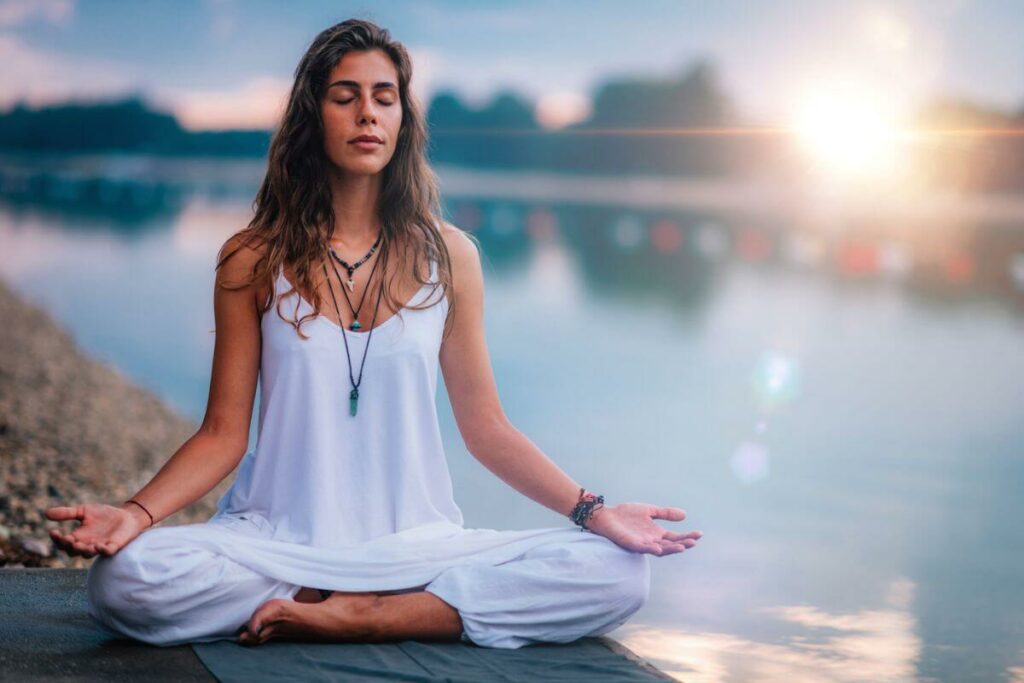 a young woman sitting on the edge of a body of water doing yoga reflecting about how mindfulness changed my life