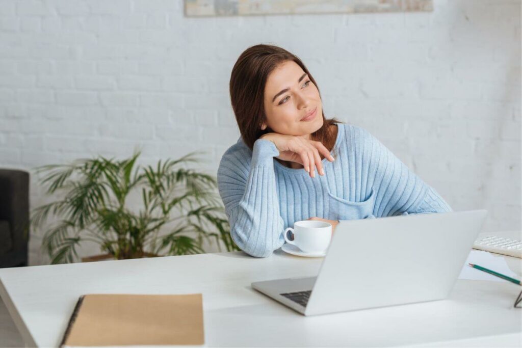 a young woman sitting at her desk happily looking off in the distance with a cup of coffee thinking how mindfulness has changed my life