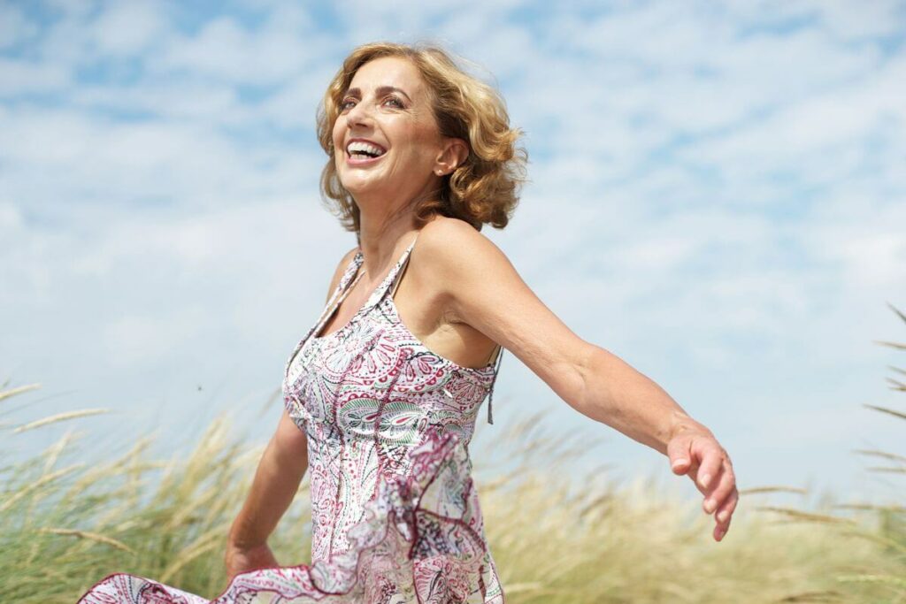 middle aged woman joyfully dancing in a field on a sunny day