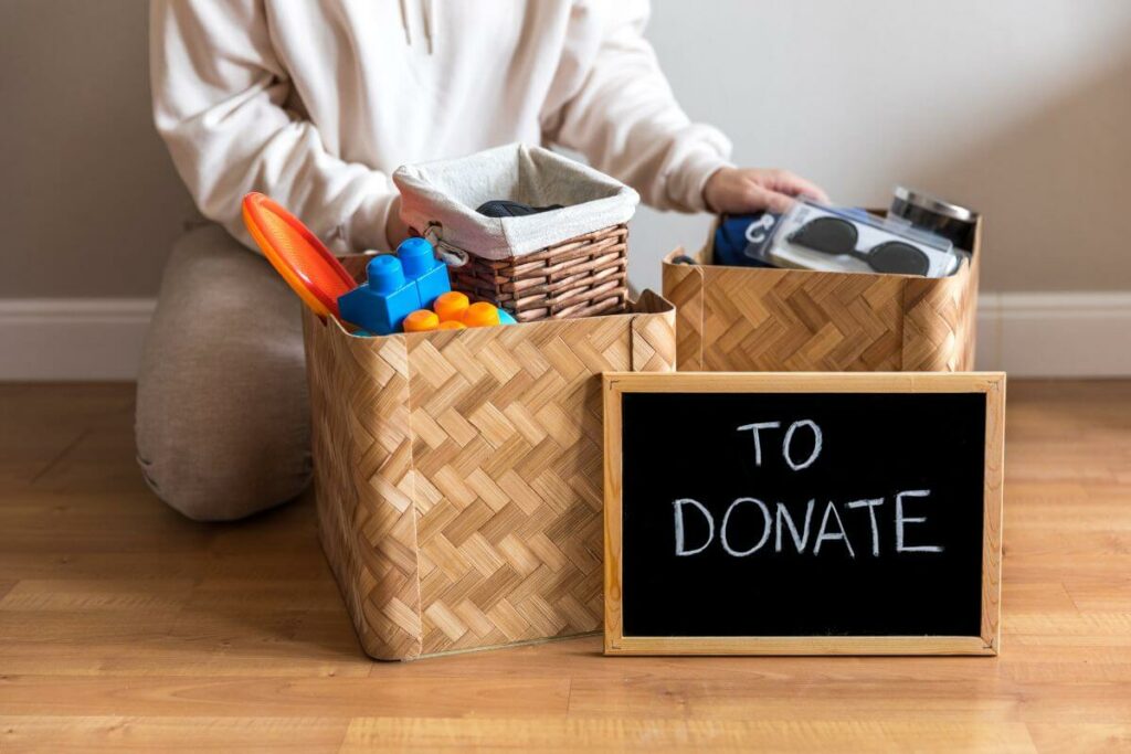 a close up of a female kneeling next to two boxes of stuff with a sign that reads To Donate.