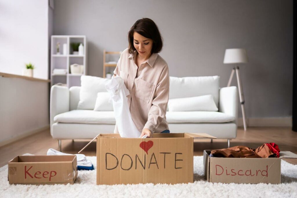 a female kneels on the floor with three boxes in front of her that read Keep, Donate, and Discard as she organizes and declutters.