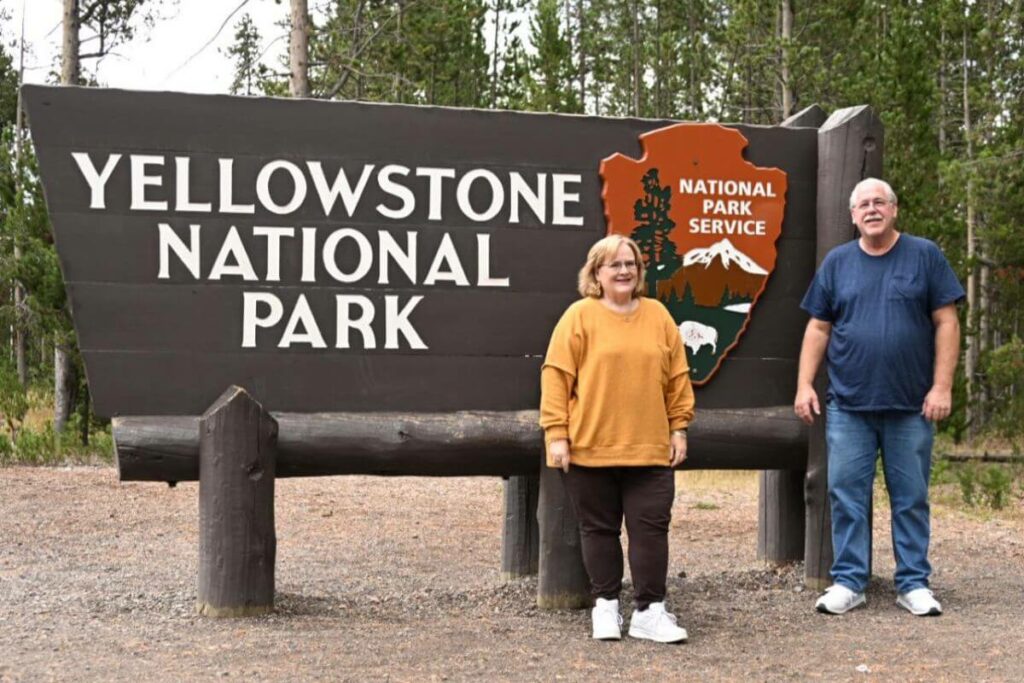 man and woman standing in front of a Yellowstone National Park sign