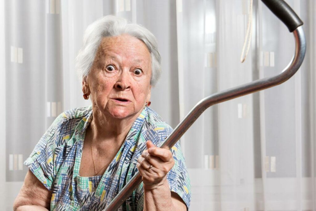 angry female senior citizen holds her cane up in the air are she argues with someone.