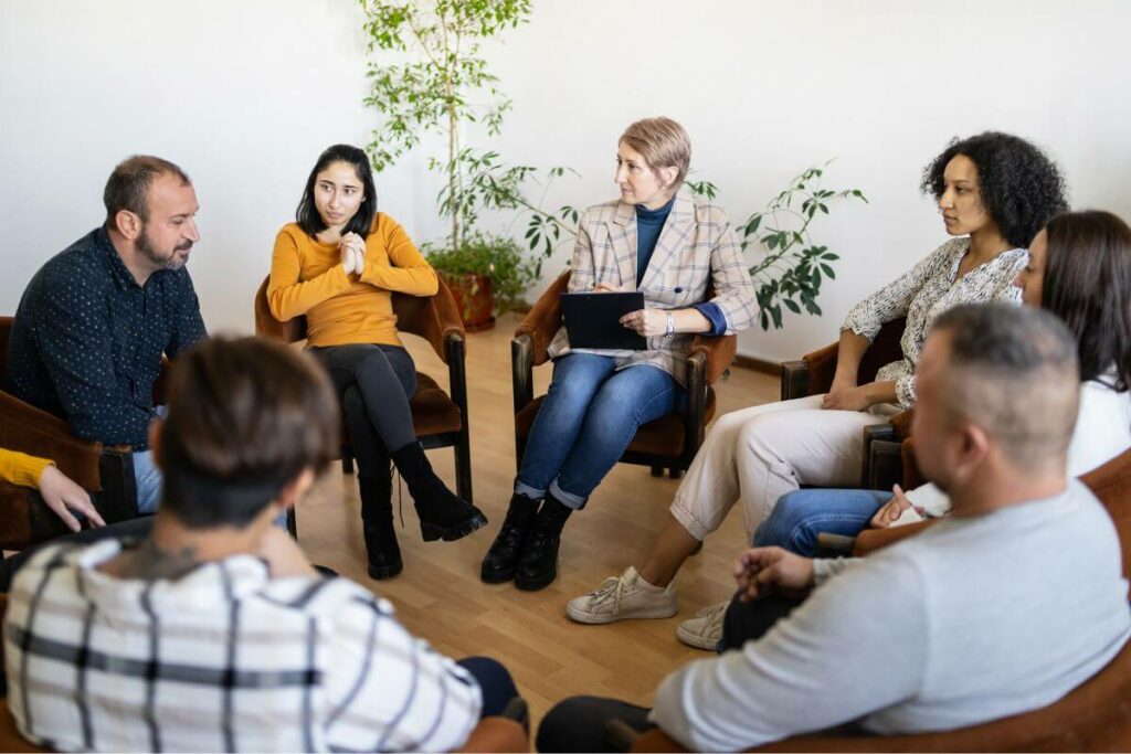 a circle of 8 people meeting with a therapist to discuss navigating family dynamics in caregiving.