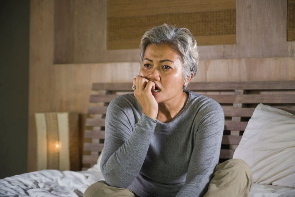 middle aged woman sits cross legged on her bed pondering how to navigate family dynamics in caregiving for her elderly parents.