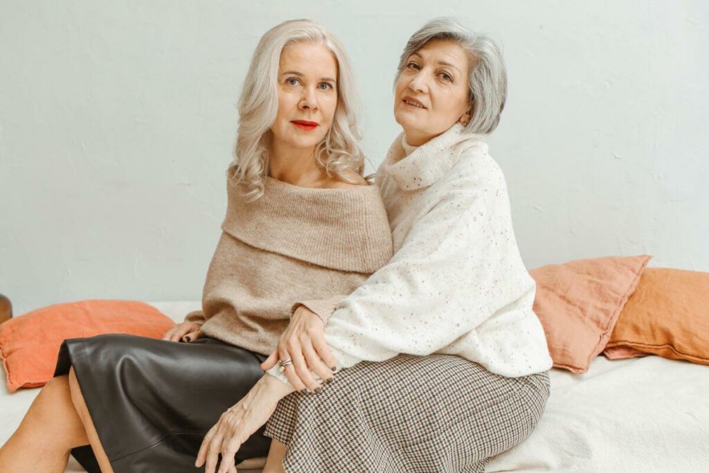 two senior women pose stylishly in adaptive clothing as they prepare to enjoy dinner with friends.