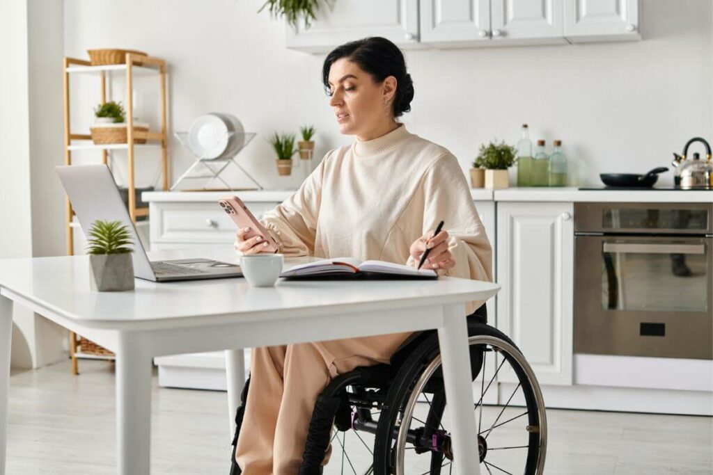 a young physically disabled woman , dressed stylishly in adaptive clothing, sits in a wheel chair and works on a computer in her beautiful home.