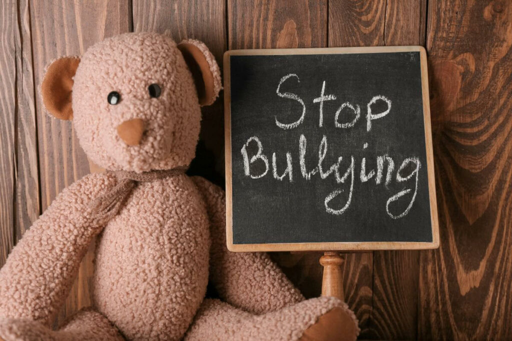 plush teddy bear laying next to a small chalkboard that says stop bullying.