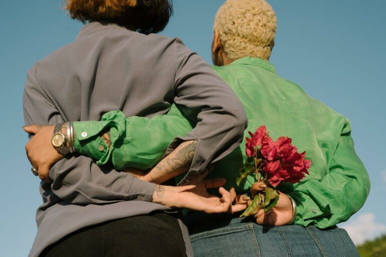 the back of two women who are holding on to each other, one with flowers in her hand.