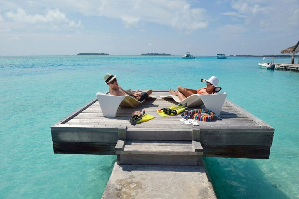 a senior couple relax together over tropical waters on a wooden platform.