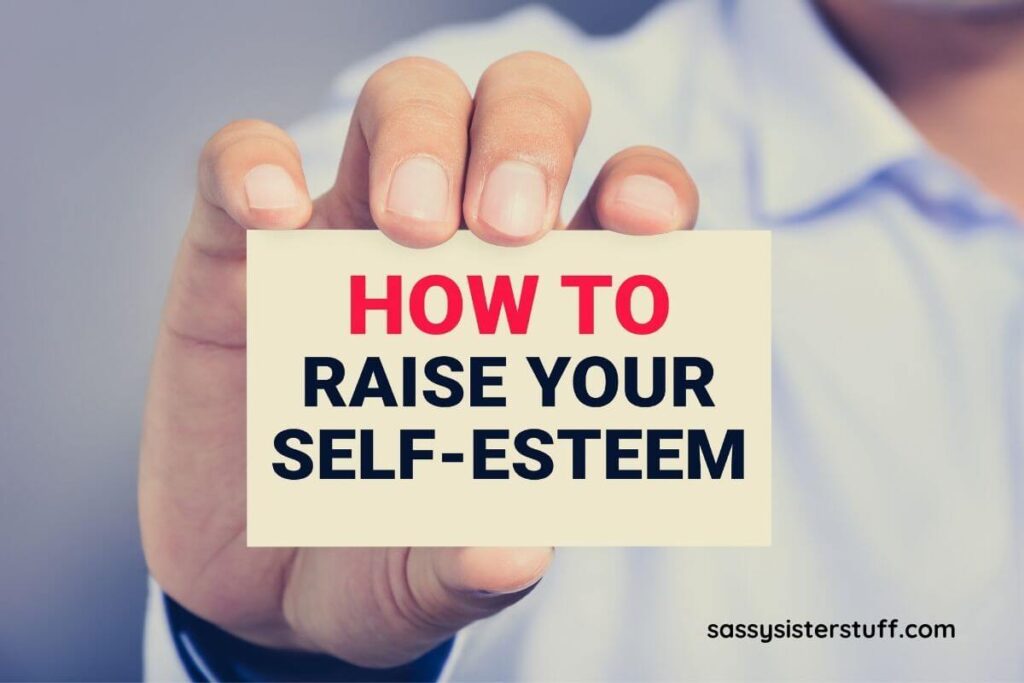 a hand holding a small sign that says How to raise your self-esteem.