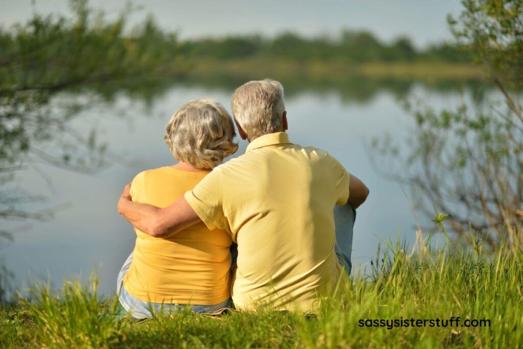 a back view of an elderly couple sitting together on the shore of a lake