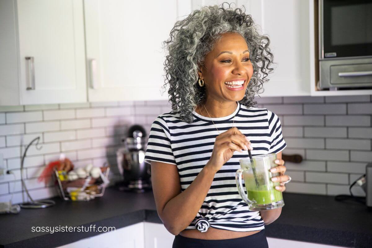 a beautiful, happy, and confident black middle aged woman drinks a green health drink