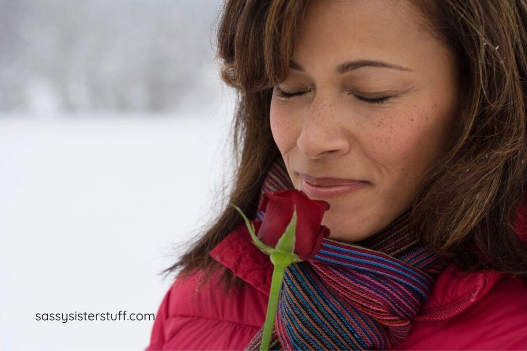 a middle aged woman smells a pretty red rose with a smile on her face