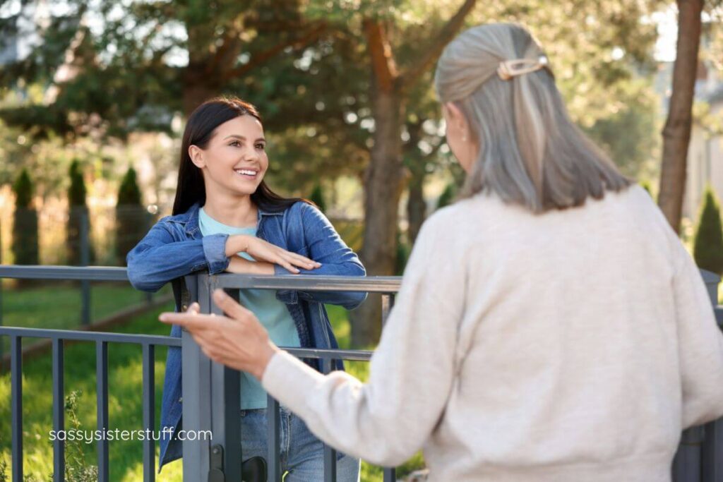 a gray haired woman stands at a fence chatting with her neighbor because she knows it's important to show kindness to her neighbors