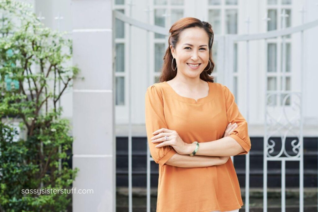 a fashionable middle aged woman smiles in front of her apartment building