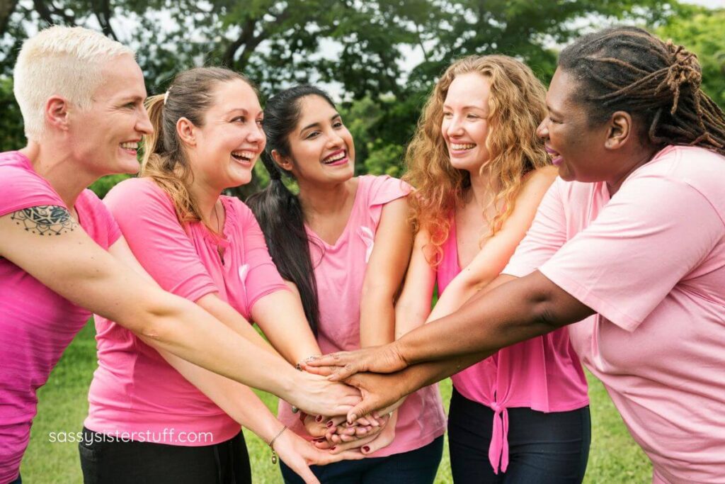 five happy woman in pink shirts put them hands together in a circle to shows unity in their common interests