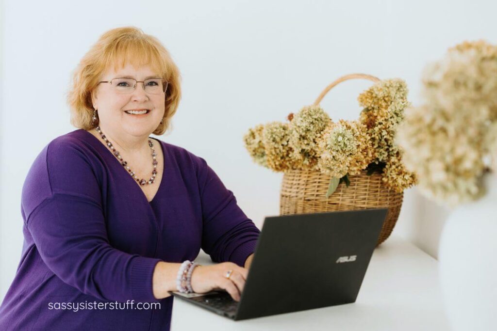 author of the blog article, life lessons i learned in midlife, smiles at the camera and types on her laptop with fall hydrangeas in the background