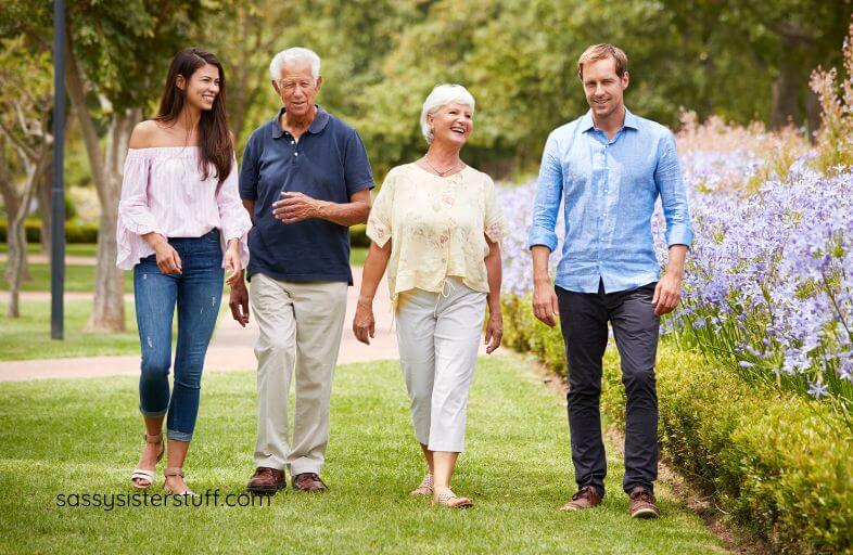 adult children and their aging parents take a pleasant walk in a park while chatting.