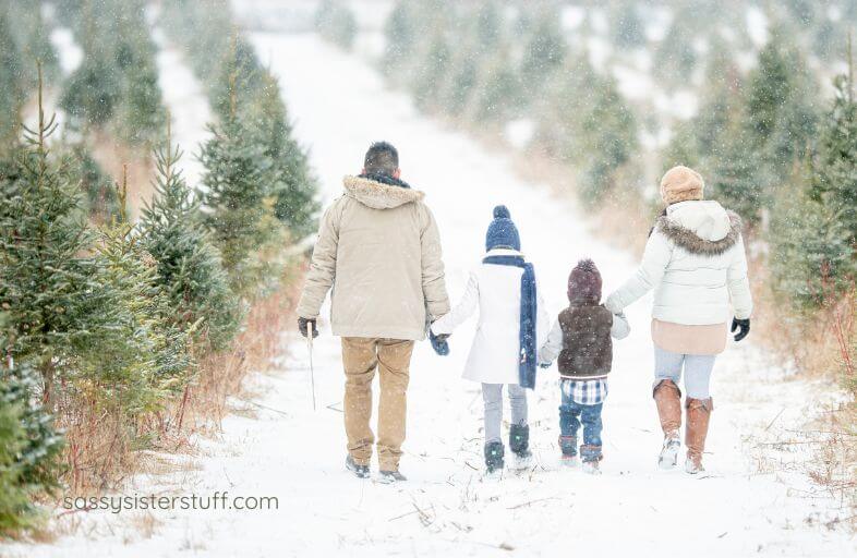 two adults and two children meander through a snowy forest together, making memories.