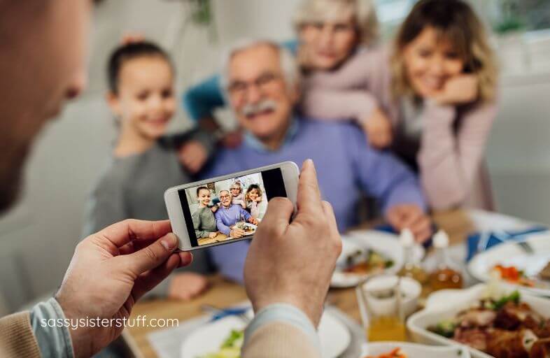 a close up of someone holding a phone camera to take a picture of a multi-generational family gathering.