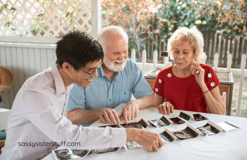 two older adults and a young man look at photos together.