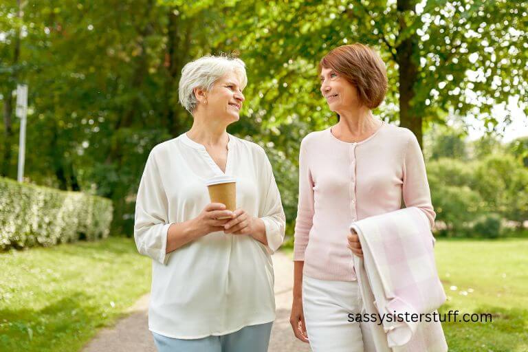 two older women casually walk through a park on a beautiful spring day.