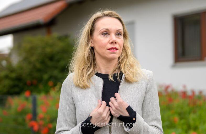 middle aged woman stands outside a home looking after something that she envies.