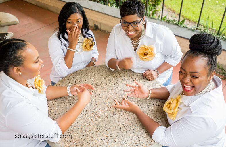 four middle aged women laugh together at a meeting as they plan conversation starters for seniors they work with.