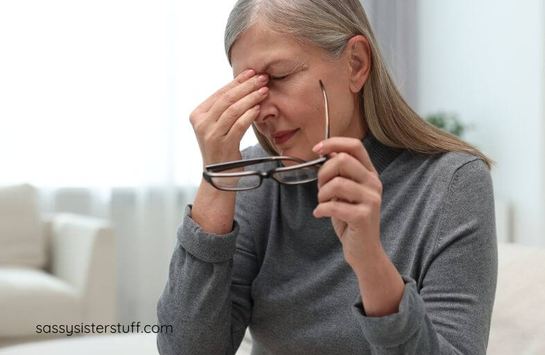 woman with glasses in hand rubbing the bridge of her nose and her eyes from fatigue