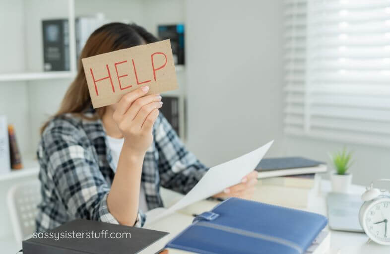 woman at desk with a sign in her hand that says HELP