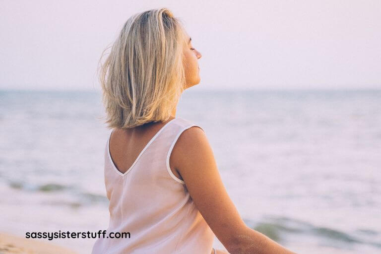 a blonde woman sits on the beach and does yoga after reading miracle of mindfulness quotes to learn to stay mindful.